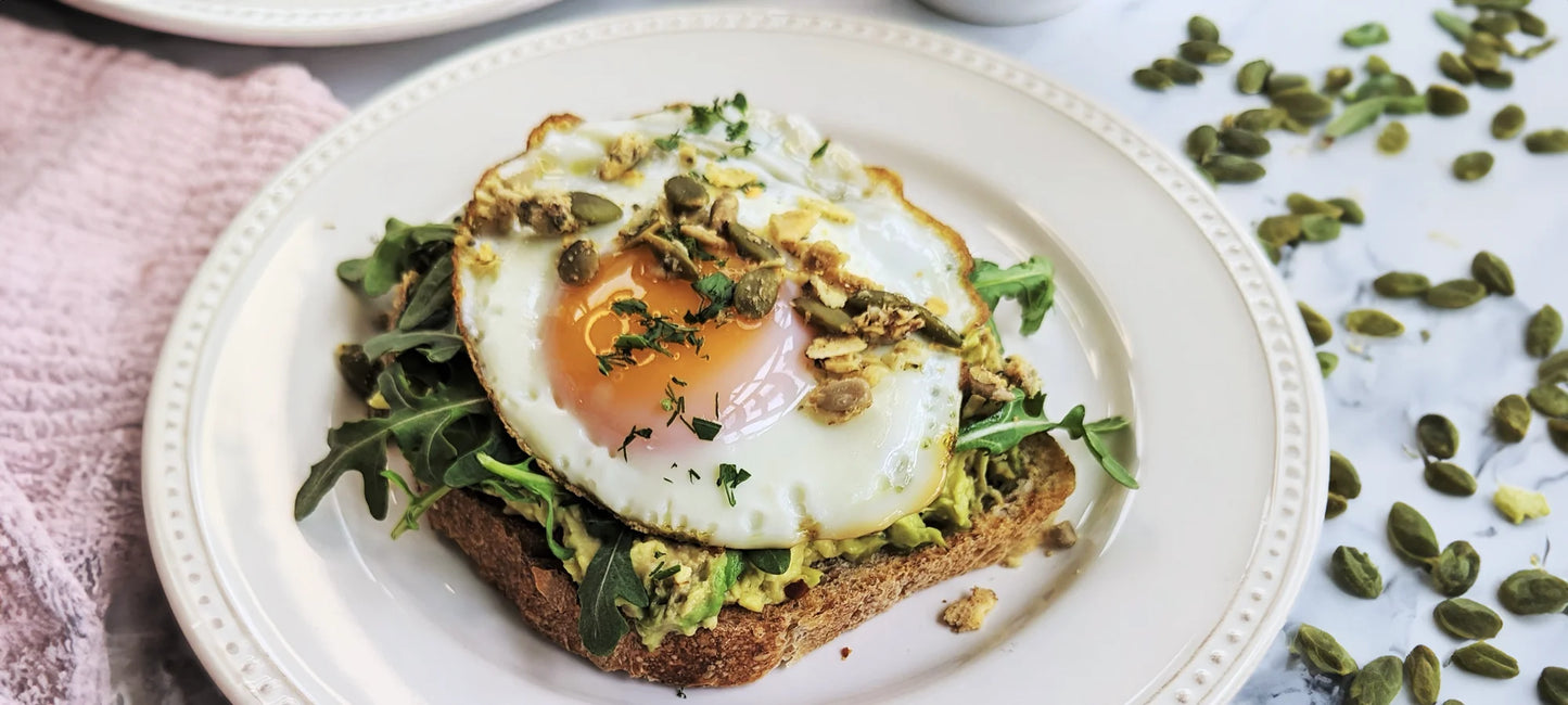 An avocado toast topped with a fried egg and Struesli's savory + seed granola.