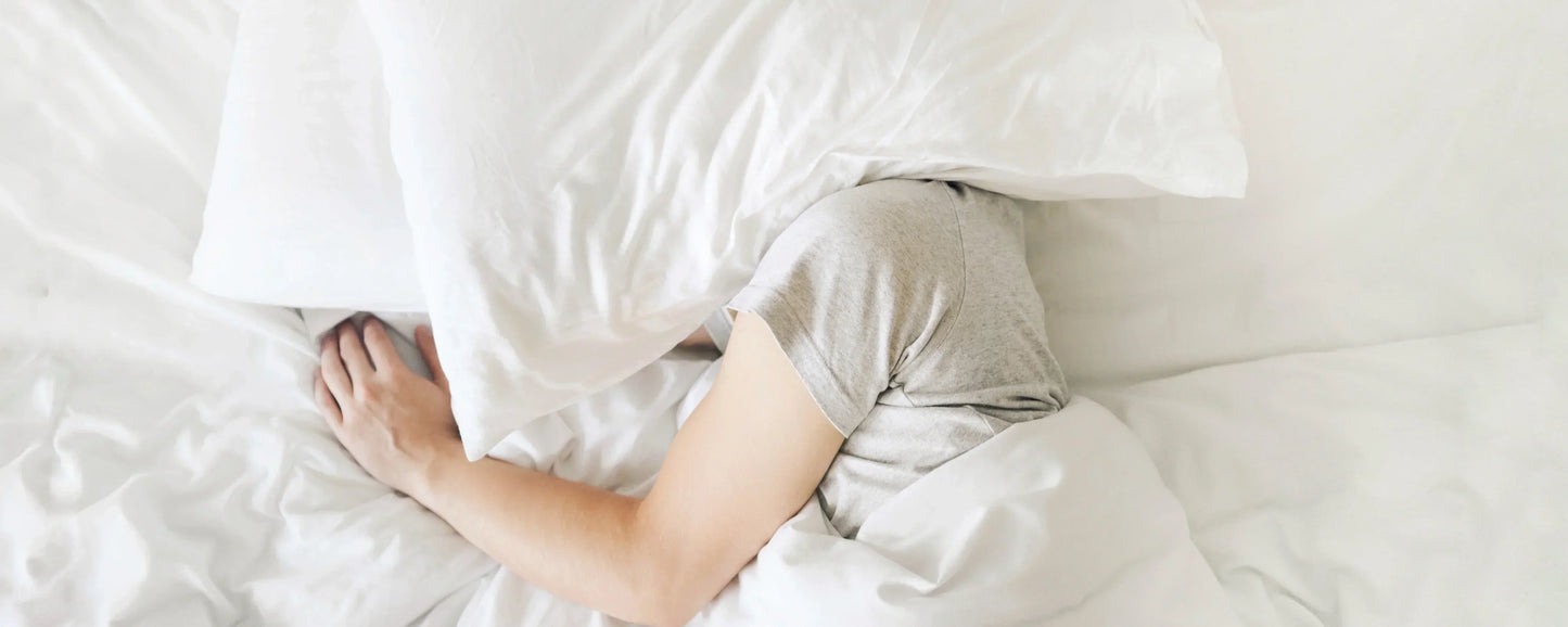 Migraine Sufferer in bed with a pillow over his/her head to block out light