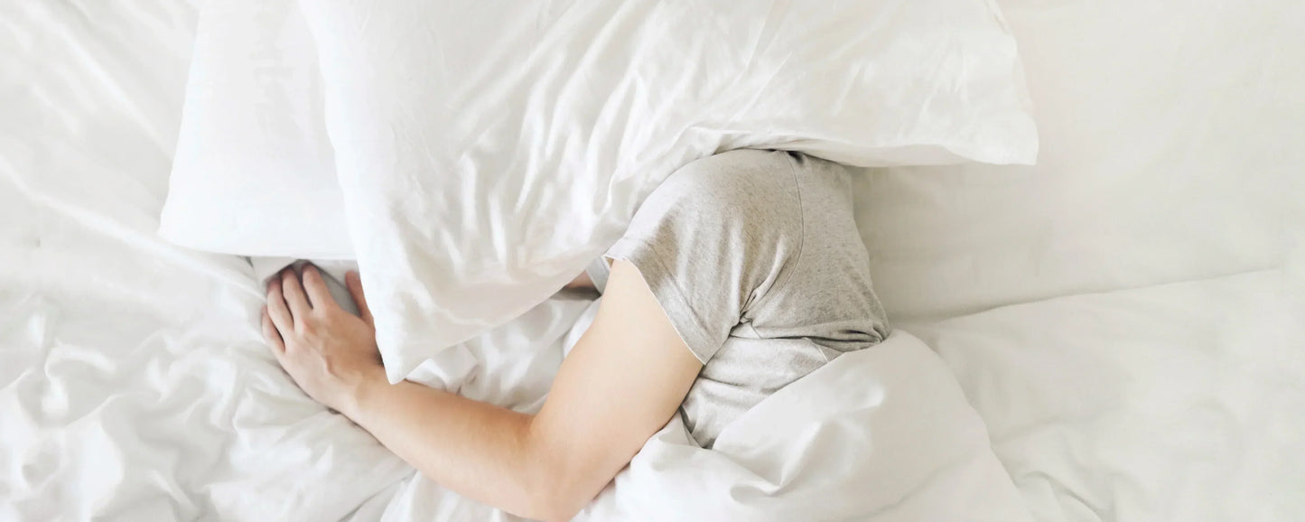 Migraine Sufferer in bed with a pillow over his/her head to block out light