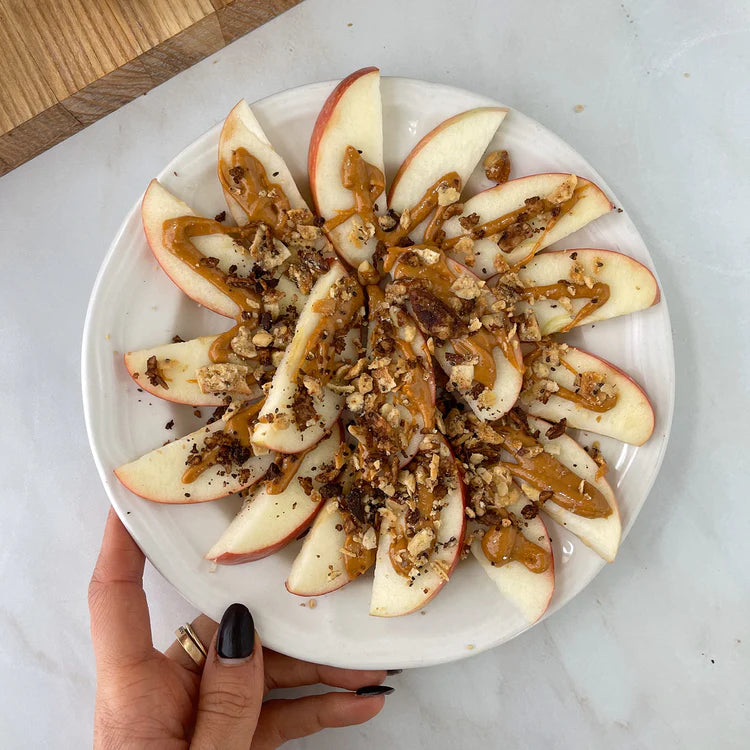 A plate of sliced apples topped with satisfying nut butter and crunchy struesli granola.