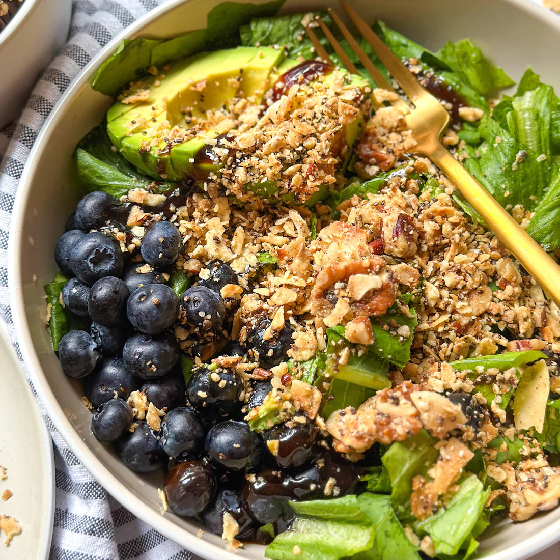 A bowl of plant-based summer crunch salad made with avocado, blueberries, leafy greens and Struesli's organic granola.