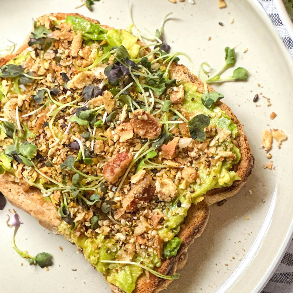 One slice of avocado toast topped with micro greens and struesli's original granola.