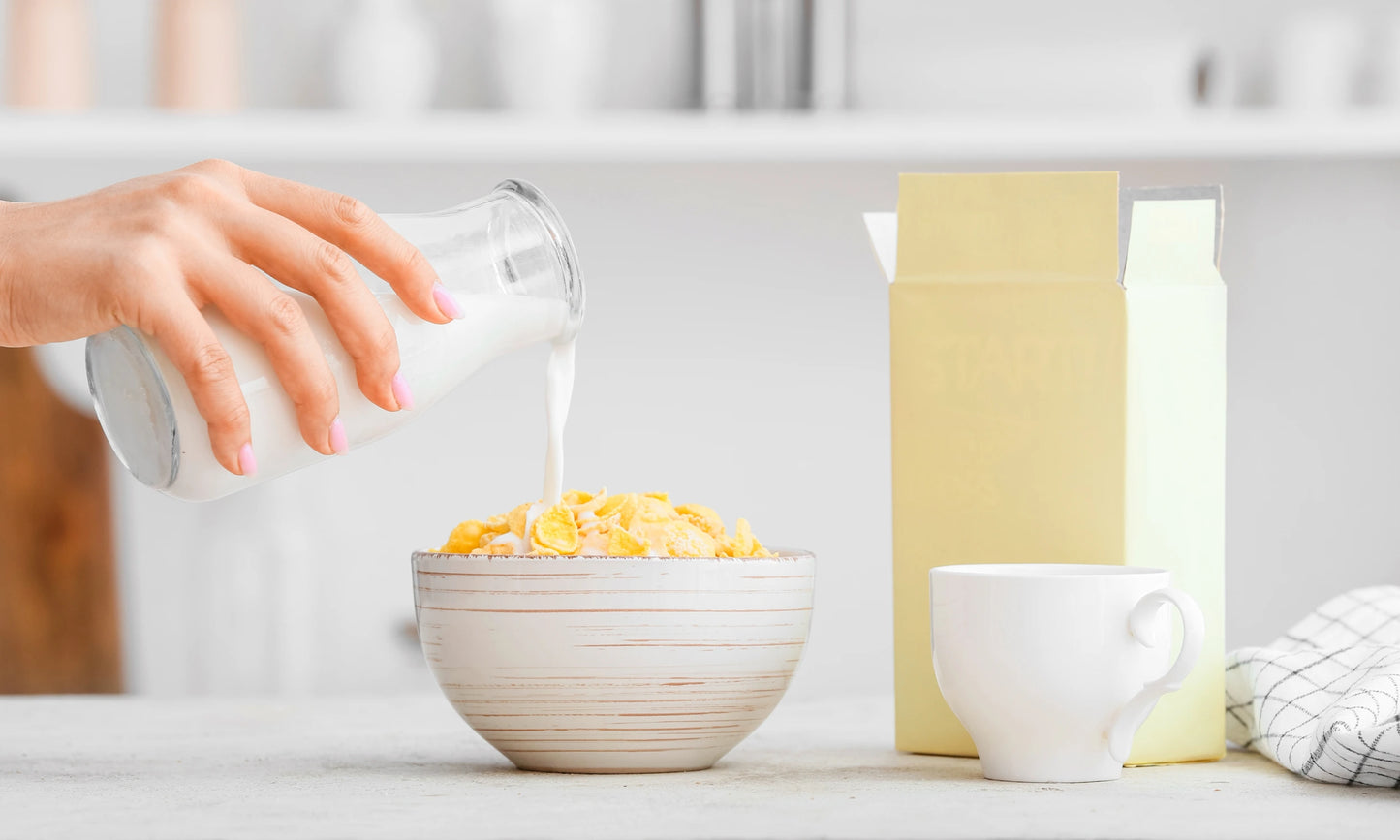 A hand pouring milk over a bowl of cereal.