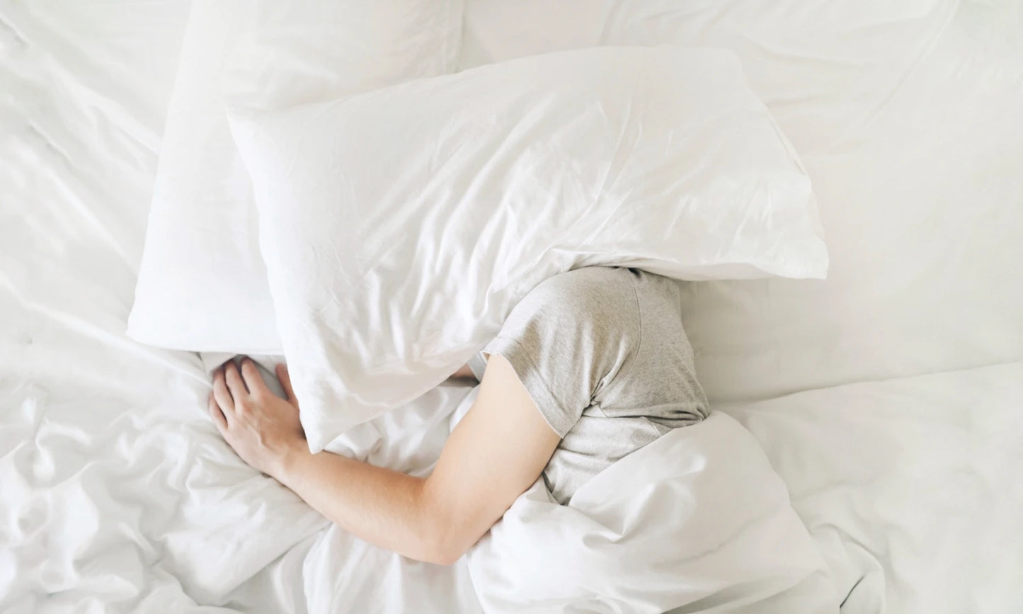 Migraine sufferer in bed with a pillow over her/his head to block out the light