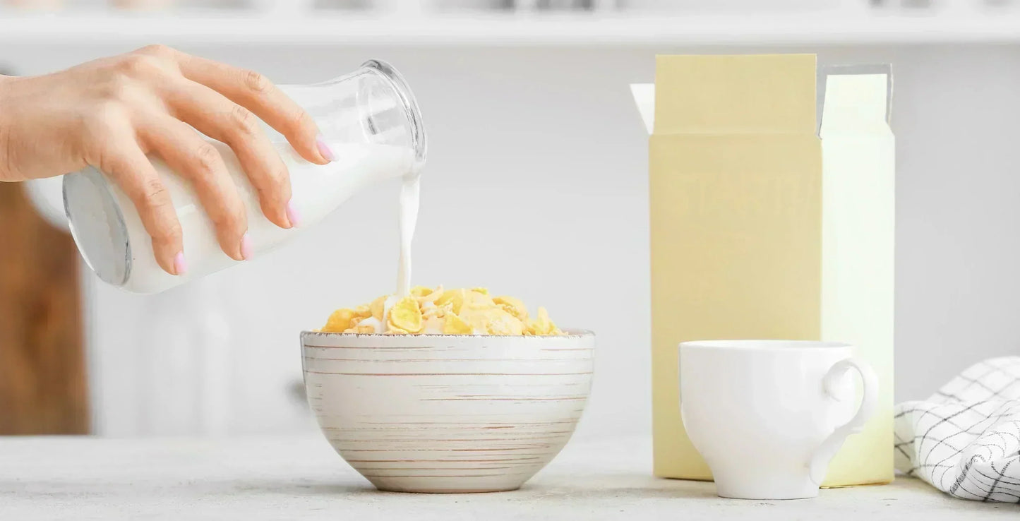 A hand pouring milk over a bowl of cereal.