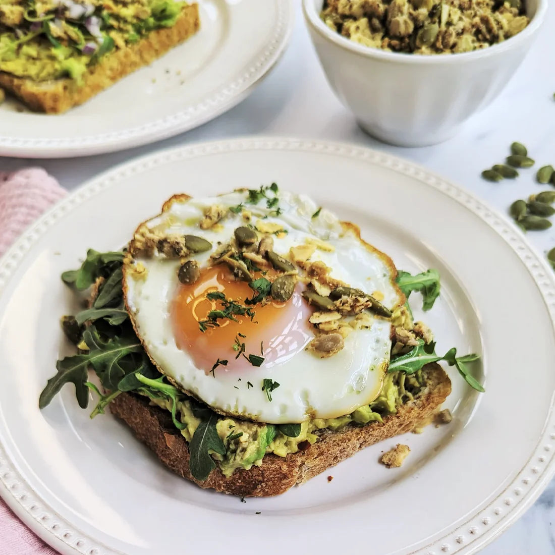 Elevated avocado toast with greens and jammy egg and a sprinkle of granola.