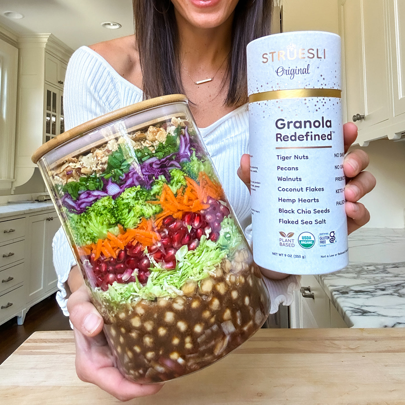 Woman holding a layered salad in a jar and a container of Struesli Original