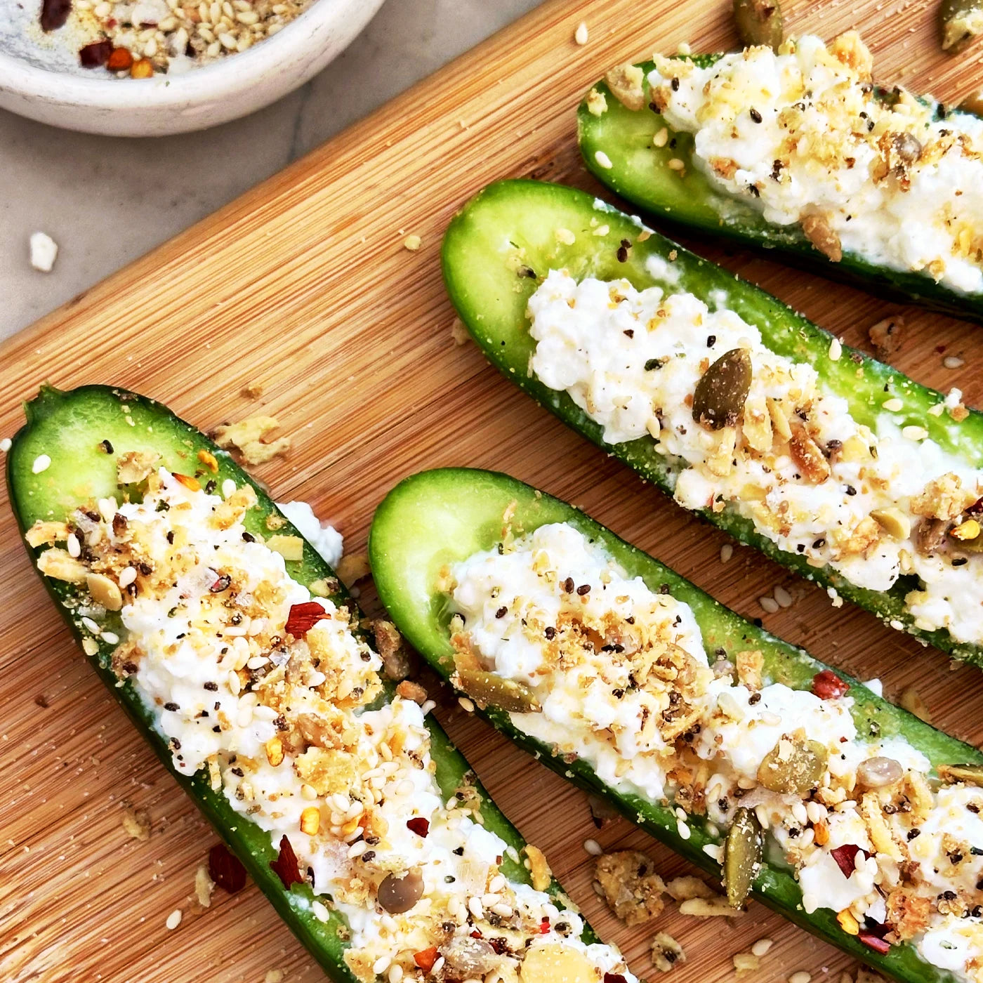 A row of sliced cucumbers topped with cottage cheese and Struesli Savory + Seed granola